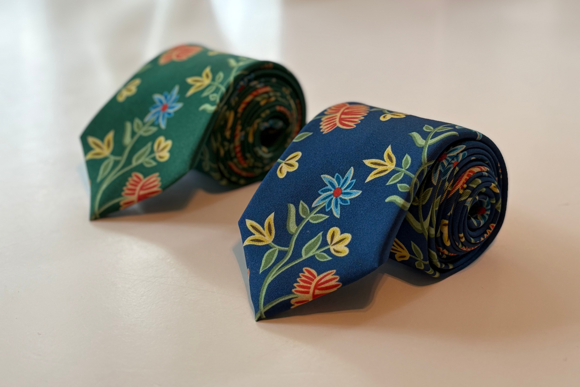 Two rolled-up floral-patterned ties on a light background